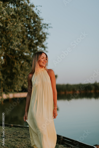 Woman walks by the water during sunset wearing a light dress at a lakeside location