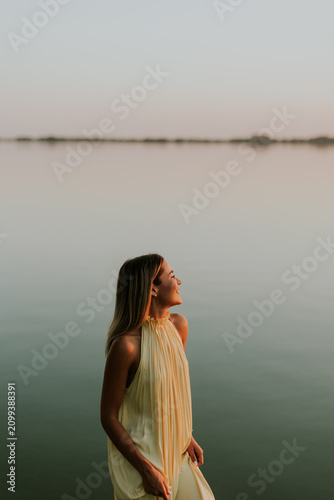 Woman stands by lake during sunset looking towards water and horizon