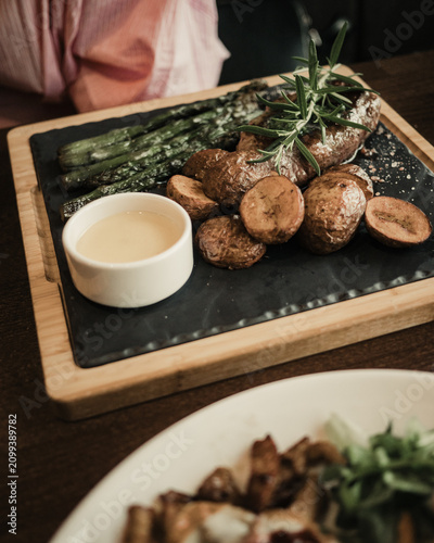Delicious grilled beef steak served with roasted potatoes, green asparagus and sauce on a black stone board, restaurant food styling, culinary lifestyle