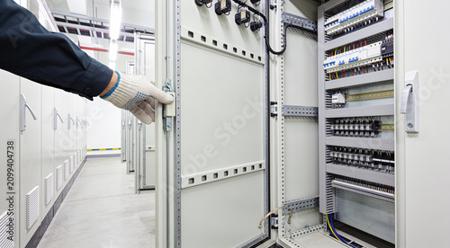 Quadro su tela Electrician's hand opening an electrical control panel in a modern facility
