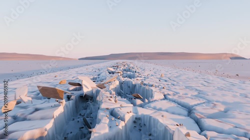 Moving camera gliding across cracked salt plain at sunrise showing deepening fissure with slabs