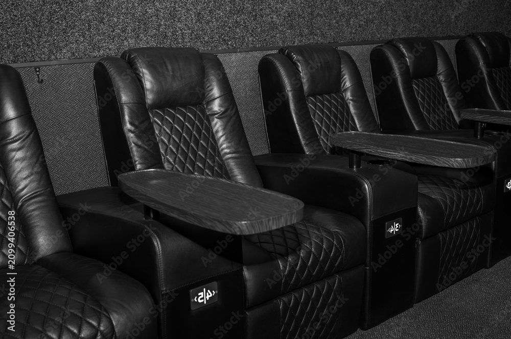 Obraz premium Luxury black and white VIP cinema seats with leather recliners and wooden trays. Premium theater interior for private screening. Elegant monochrome furniture