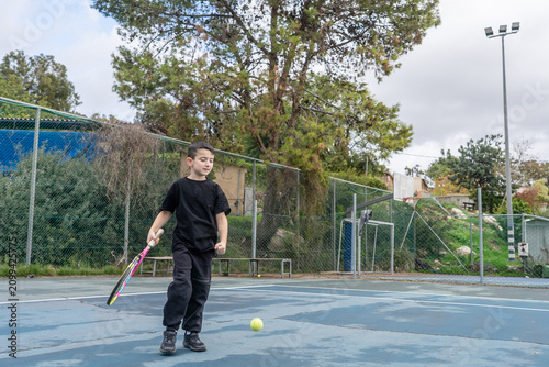 Bild auf Leinwand A boy stands on a tennis court holding a racket