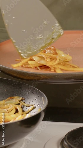 Vertical video: Scooping cook in olive-apron with clay plate over pan, plating strips with spatula