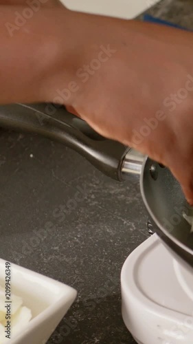 Vertical video: Entering hand scooping onions from bowl into pan, adjusting handle on plate to cook