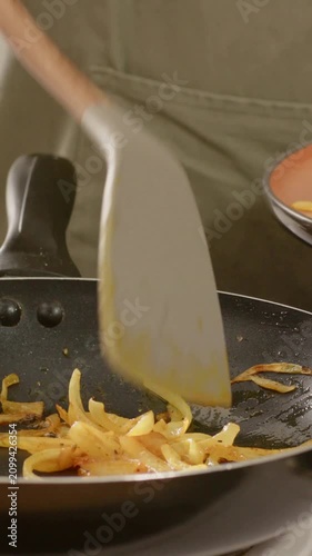 Vertical video: Sizzling onions as cook in light apron stirring scraping scooping to plate at stove