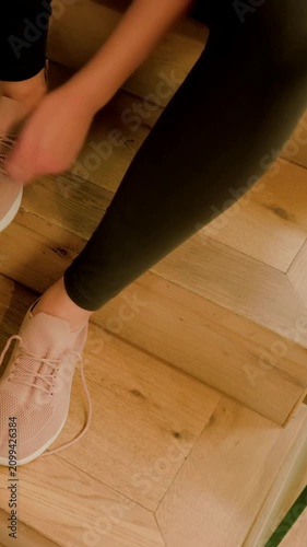Vertical video: Placing feet, she in leggings tying pink sneaker laces on wood steps to leave