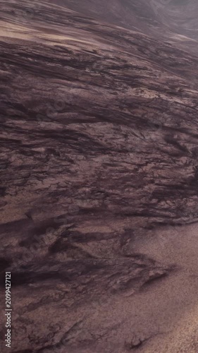 A dry lava field shows black rock formations with textures and patterns. The area is mostly barren with shades of tan soil visible. The landscape appears rugged and uneven.