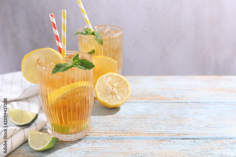 Fototapeta premium Refreshing ice tea with lemons, lime and mint on wooden table, closeup. Space for text
