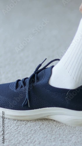 Vertical video: Reaching mint sleeve hand guiding white sock into navy shoe at home, leaving