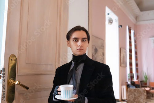 Aristocrat man drinking coffee in historical interior. Young philanthropist holding cup. Wealthy intellectual man in retro costume. Elegant refined lifestyle luxury concept portrait.