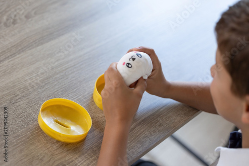 Foto Young child grips white squishy toy with printed cartoon face beside open yellow
