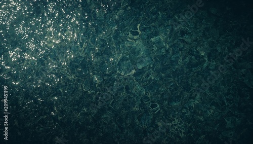 Water Surface With Sunlight Reflecting on Dark Ocean Floor Filled With Marine...