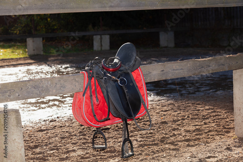 horse saddle hangs on wooden fence in farmyard