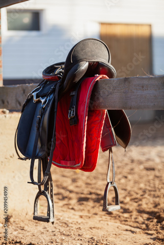 horse saddle hangs on wooden fence in farmyard