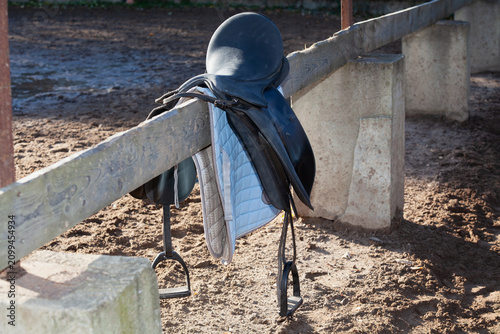 horse saddle hangs on wooden fence in farmyard