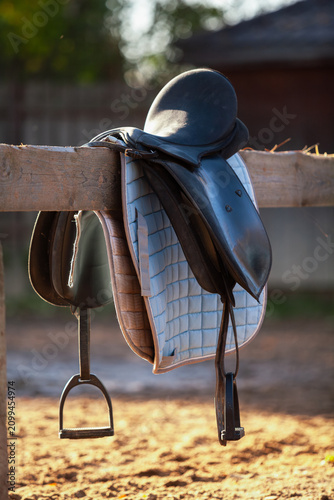 horse saddle hangs on wooden fence in farmyard
