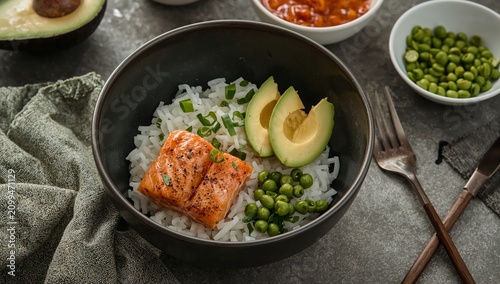Bowl With Rice, Salmon, Avocado, and Green Peas on a Table With Utensils and ...