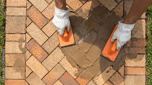 Grouting bricks on outdoor patio using rubber float with flooring construction hardscape