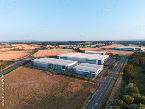 Aerial View of Modern Industrial Warehouse Complex in Green Countryside at Sunset – Commercial Buildings in Rural Setting