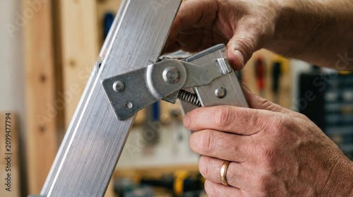 Hands adjusting the metal hinge mechanism on an aluminum folding ladder