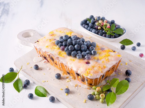 Homemade lemon blueberry loaf cake with homegrown blueberries  and lemon zest on a white cutting board; copy space