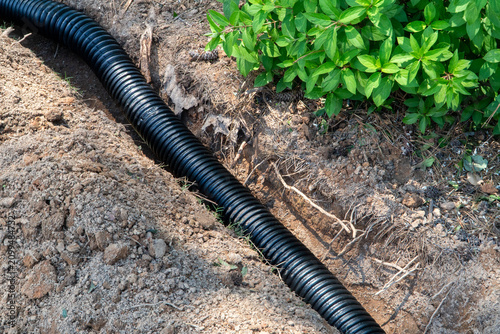 Obraz na plátně Installing a black corrugated flexible drainage pipe in an excavated trench, surrounded by disturbed soil, exposed roots, and lush green plants, ready for efficient storm water management