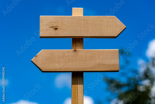 Blank wooden directional signpost with opposite arrows against blue sky, closeup. Empty wooden sign board with two arrows pointing left and right over bright blue sky background ready for copy space