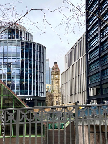 BIRMINGHAM, UK - A framed urban view of the historic Big Brum clock tower, positioned between modern glass and steel office buildings in Chamberlain Square.