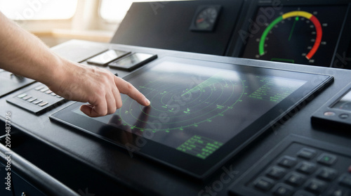 Hand operating a digital marine radar touchscreen for ship navigation, vessel tracking and maritime safety on a modern bridge control console.