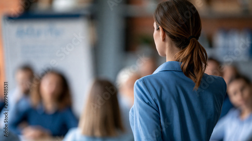 Faceless female life coach facilitating a goal-setting workshop with a group of aspiring professionals, flip chart with action plan visible, defocused workshop room in background,