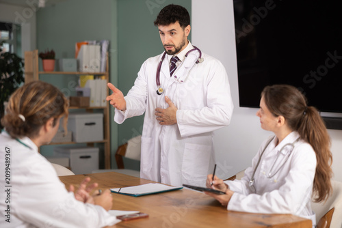 Bild auf Leinwand Positive male physician in white coat instructing medical staff during education