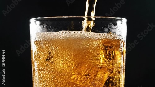 Golden amber soda pours into a tall glass filled with crushed ice, creating refreshing condensation and effervescent bubbles under high-contrast commercial lighting against a dark background.
