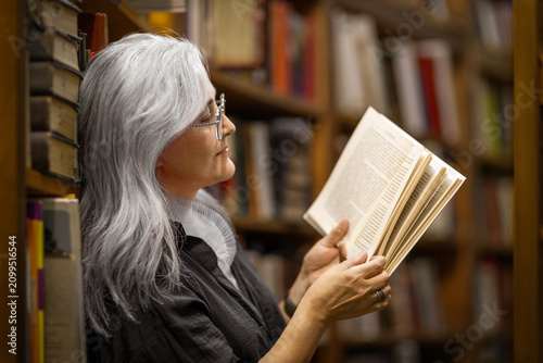 Senior woman reading book in library, enjoying quiet knowledge