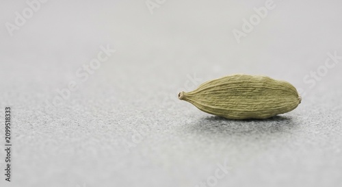 Single organic green cardamom pod on light granite minimal food stock