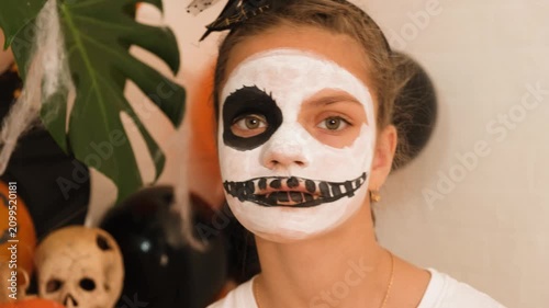 A cute teenage girl is getting ready for Halloween and doing face painting, with a skeleton painted on her face. October is a time of horror.