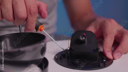 Hands tightening screw on black plastic component with screwdriver during careful repair work on white tabletop with shallow focus and close detail view, with screwdriver, hand, screw, repair detail