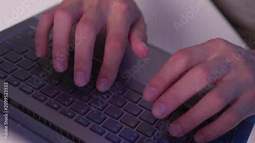 Hands typing on laptop keyboard in close view with fingers pressing keys, subtle movement and focused work at desk under cool indoor light during office routine