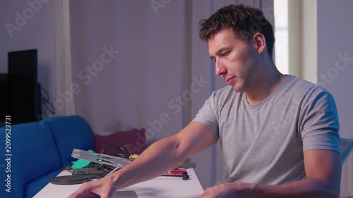 Young man typing on laptop at home desk with focused posture, subtle hand movement and soft mixed lighting in comfortable workspace, showing quiet remote work concentration and evening routine
