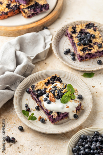 Blueberry baked oatmeal piece with greek yogurt topping served on ceramic plates, beige textured background