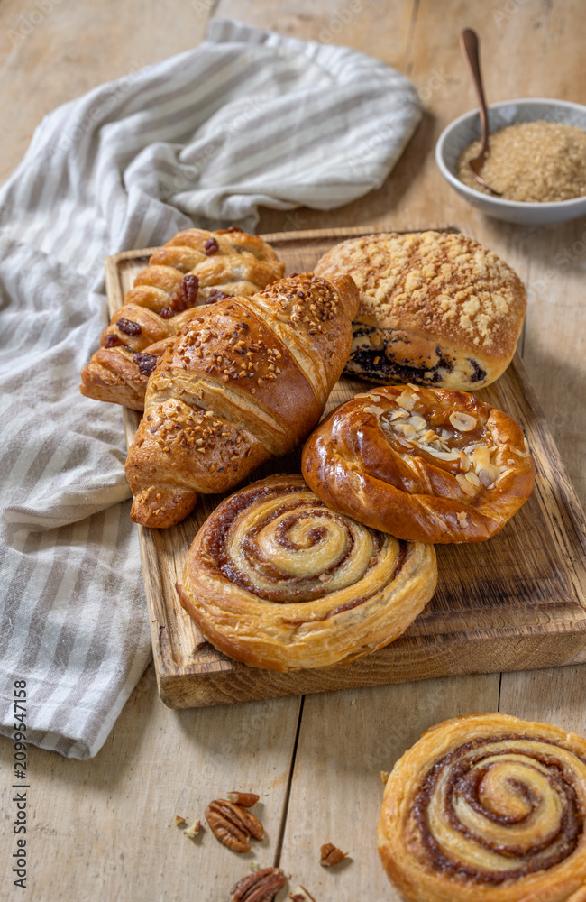Fototapeta premium Various Freshly Baked Sweet Buns on Rustic Wooden Table and Cutting Board