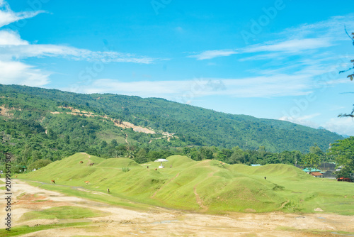 Photography Scenic view of lush green rolling hills under a bright blue sky with scattered c