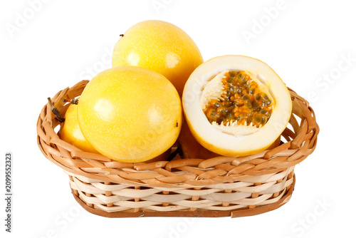 Fresh yellow passion fruits arranged in a wicker basket with one sliced fruit showing juicy pulp and seeds, isolated on a white background