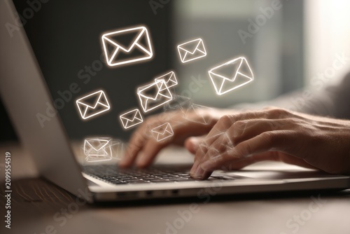 Close-up of hands typing on a laptop, with glowing email icons floating above, signifying electronic communication