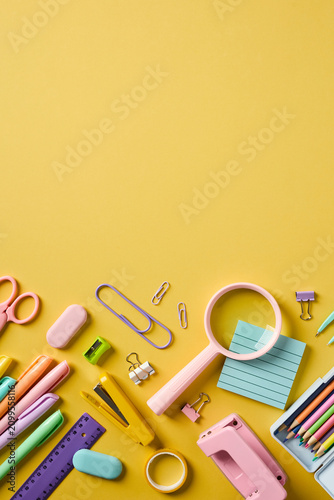 High angle view of pastel school supplies organized at the bottom of a vertical yellow background with copy space