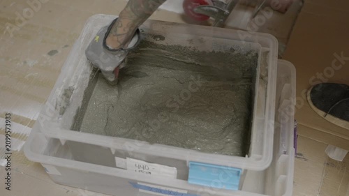 This video shows a close up of a worker wearing a protective glove using a hand trowel to mix mortar in a large plastic bucket.