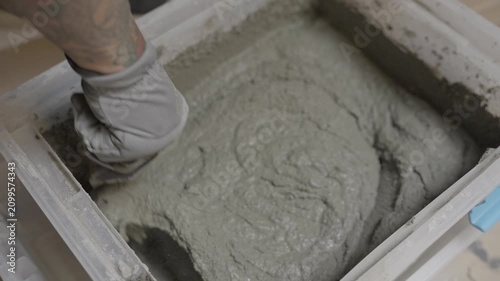 This video shows a close up, overhead view of a mason hand-mixing cement mortar with a steel trowel inside a heavy-duty plastic container.