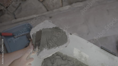 This video shows an overhead view of a worker holding a stone rock veneer upside down and slathering mortar on the back with a trowel.