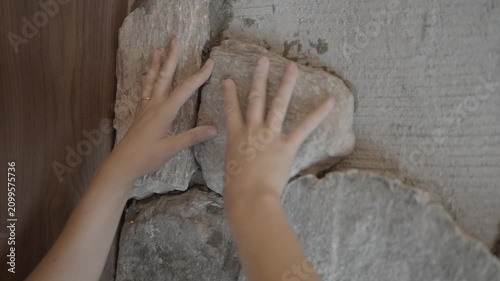 This video shows a close up view of the hands of a mason carefully placing a rock onto a stone wall with fresh mortar.