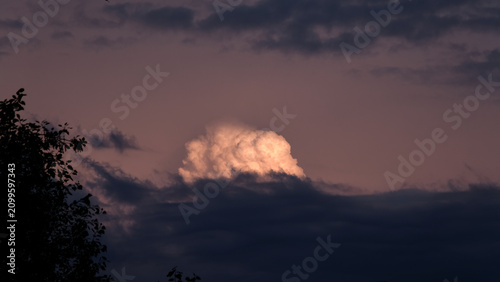 Fantastic view of storm front with single cumulus cloud glowing brightly in the last rays of the setting sun.
